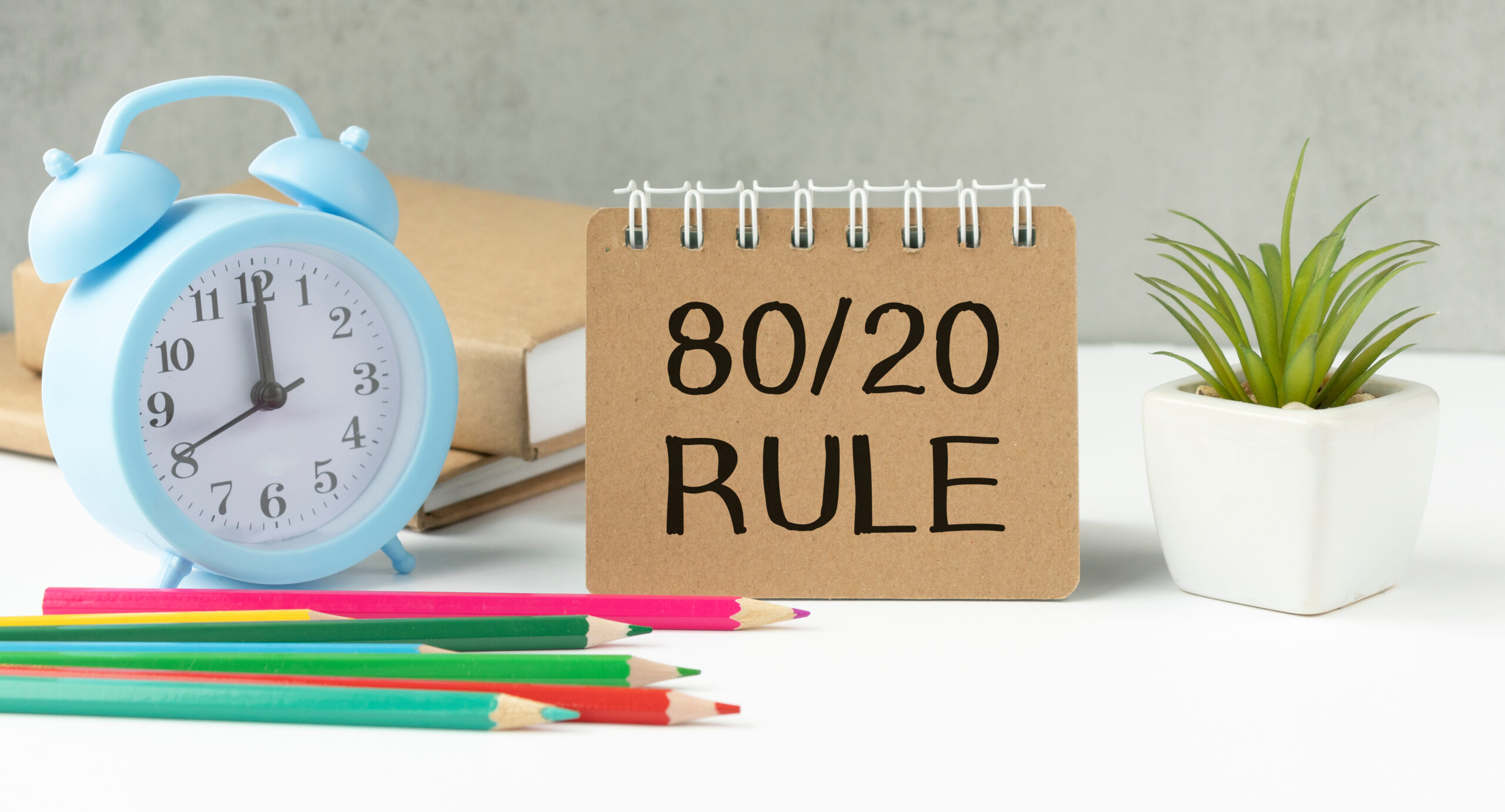 A desk setup with a notebook displaying '80/20 RULE,' a clock, and colorful pencils, symbolizing the Pareto Principle in learning—focusing on the 20% of effort that yields 80% of results.