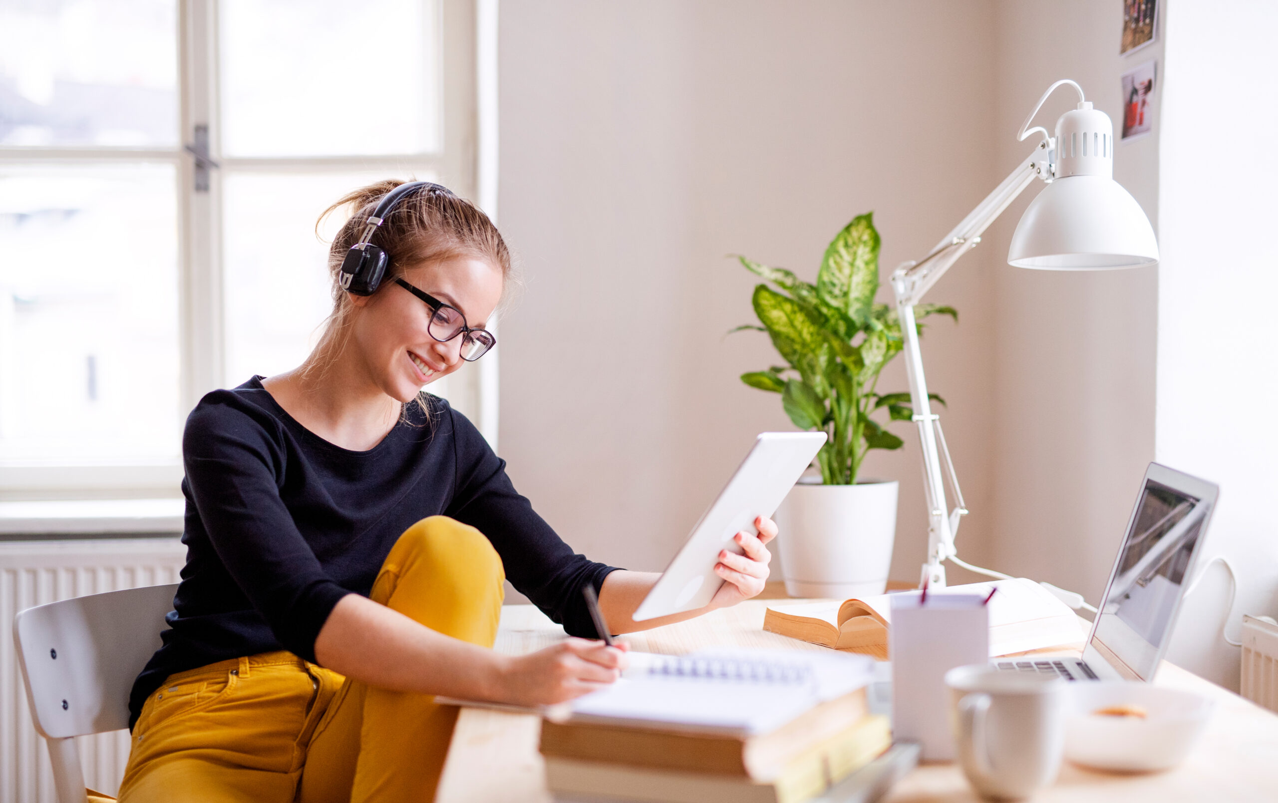 A young woman studying at a bright desk, wearing headphones and using a tablet, symbolizing how music enhances focus, learning, and cognitive performance.