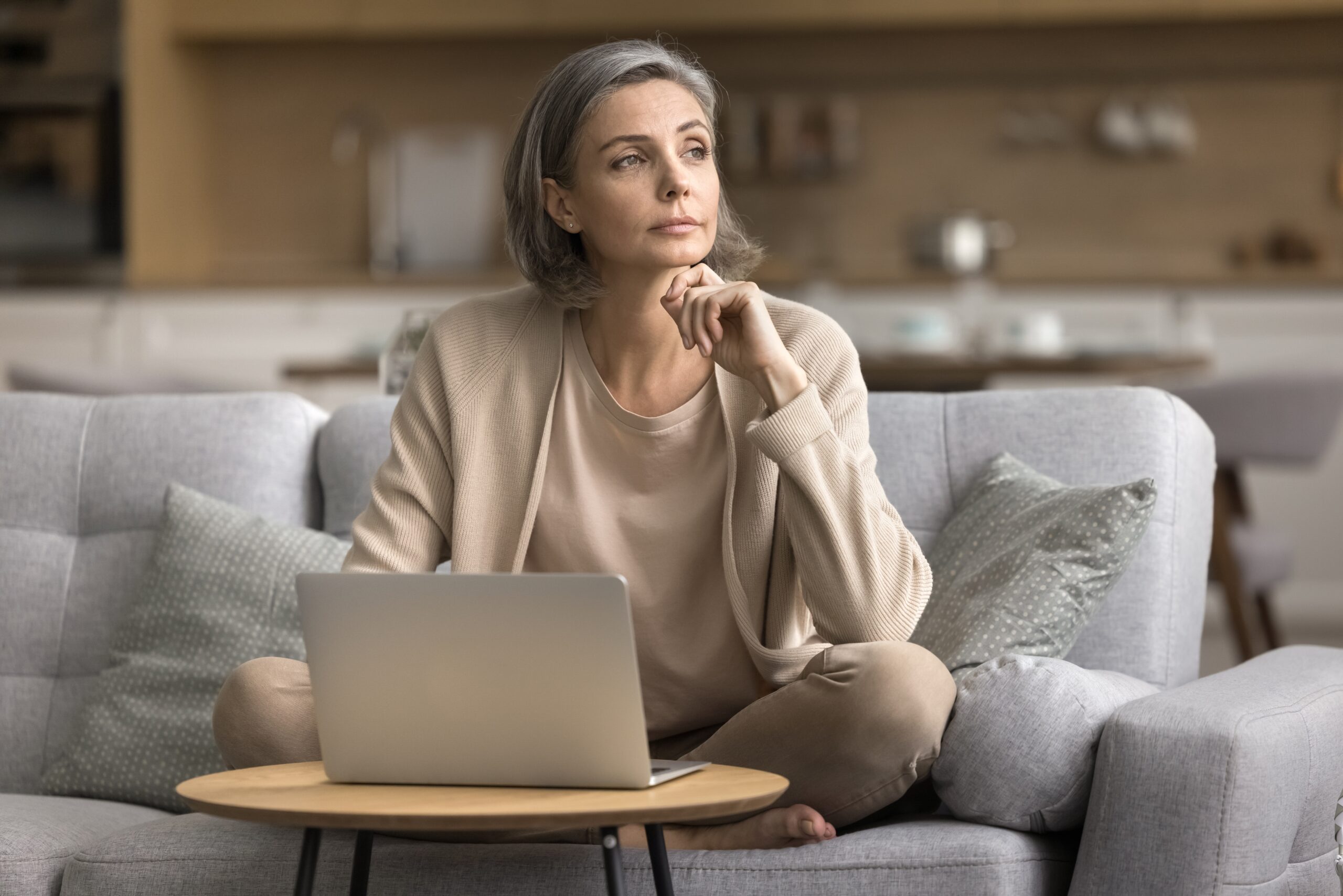 A thoughtful woman sitting on a couch with a laptop, reflecting on a decision, symbolizing critical thinking and the psychology behind making smart choices.